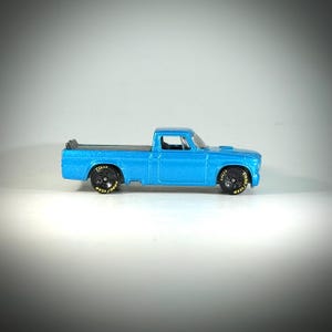 May include: A small, die-cast, light blue pickup truck with black wheels and Goodyear Eagle tires. The truck has a detailed cab and bed, and is set against a white background. The tires have yellow lettering.