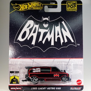 May include: A black 1985 Chevy Astro Van die-cast toy car with red trim and "The Caped Crusader" written on the side. The car is part of the Hot Wheels Premium Pop Culture series and features the Batman logo.