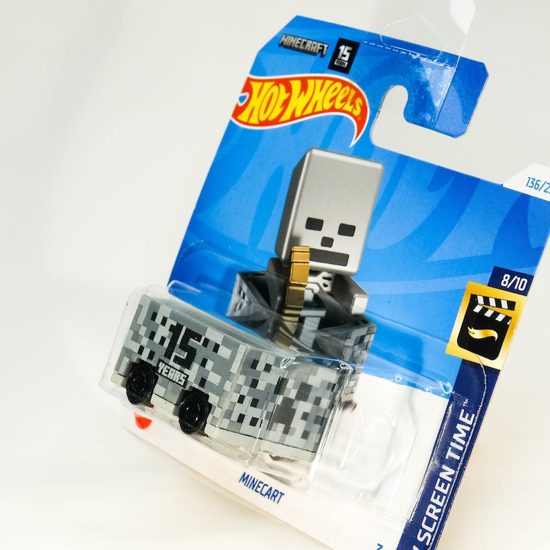Puede incluir: Un coche de juguete Hot Wheels de tem&aacute;tica Minecraft gris y blanco con una figura de esqueleto en el embalaje. El coche es un carro de mina con el texto "15 Years" en el lateral. El embalaje tiene el texto "Minecraft" y "Hot Wheels".