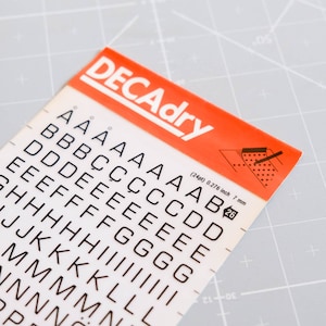 May include: A sheet of white adhesive letters and numbers on a white background. The letters are black and range from A to P. The sheet is labeled "DECAdry" in red and has a measurement of 0.276 inches or 7 mm.