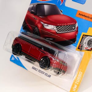 May include: Red toy car model of a Range Rover Velar with black wheels and the text "Range Rover Velar" and "HW Turbo" on the packaging.
