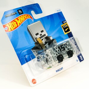 Puede incluir: Un coche de juguete Hot Wheels Minecraft 15 Years de fundici&oacute;n a presi&oacute;n con una figura de esqueleto gris que viaja en un carro de mina pixelado gris y blanco. El embalaje es azul y blanco con el logotipo de Hot Wheels y la marca Minecraft.