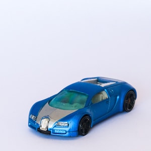 May include: A blue toy car with a silver stripe down the hood. The car has black wheels and a detailed interior.