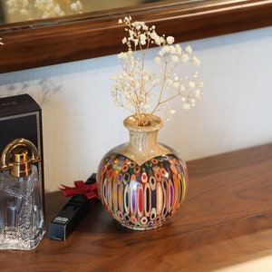 May include: A colorful vase made from pencils, with a brown wood base, filled with white baby's breath flowers.