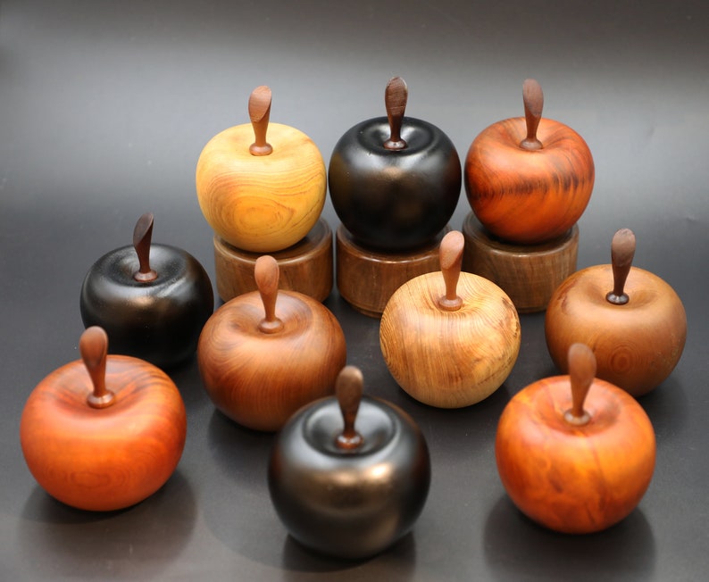 May include: A collection of nine wooden apple-shaped boxes in various shades of brown, black, and red. The boxes are arranged in a circular pattern on a black surface.