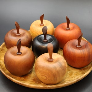 May include: Seven wooden apple-shaped boxes in various shades of brown, red, and black, arranged on a wooden tray with a burl pattern.