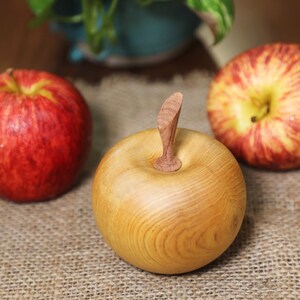 May include: Three apples, two red and one wooden, on a burlap surface. The wooden apple has a carved stem.