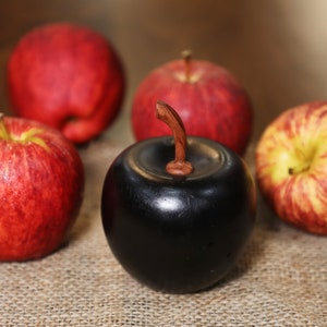 May include: Five apples, four red and one black, on a burlap surface. The black apple is made of wood and has a wooden stem.