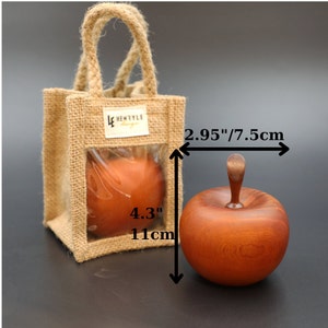 May include: A wooden apple ornament in a reddish-brown color with a smooth finish. The apple is 2.95 inches wide and 4.3 inches tall. The apple is packaged in a burlap bag with a clear window.