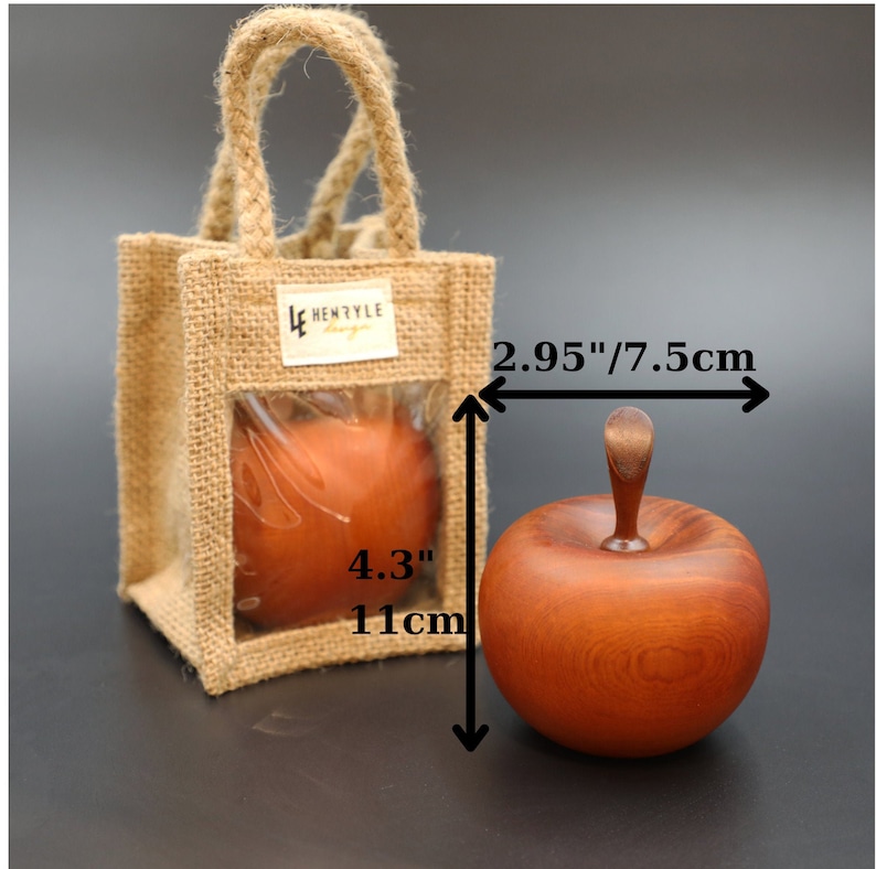 May include: A wooden apple ornament in a reddish-brown color with a smooth finish. The apple is 2.95 inches wide and 4.3 inches tall. The apple is packaged in a burlap bag with a clear window.