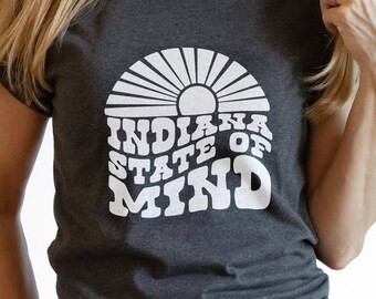 May include: A dark grey t-shirt with a white graphic design of a sun with rays and the text "Indiana State of Mind".