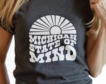 May include: A dark gray t-shirt with a white graphic design of a sun with rays and the text "Michigan State of Mind".