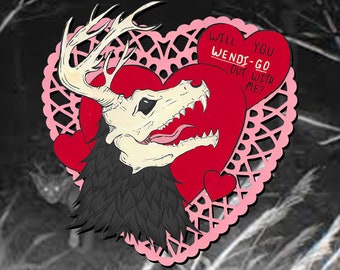 May include: A pink heart-shaped lace doily with a red heart inside. A skeletal deer head with black fur is in the center of the heart. The text "Will you Wendi-go out with me?" is written on a smaller pink heart.