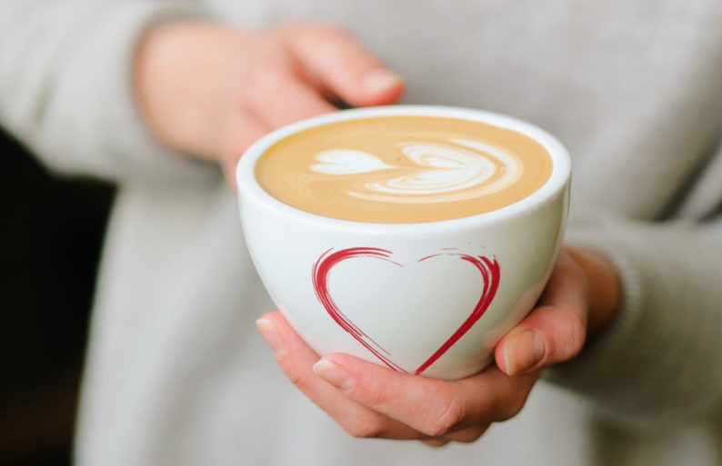 May include: A white ceramic mug with a red heart design, filled with a latte with a heart-shaped design in the foam.