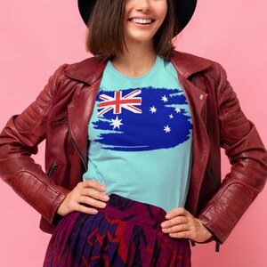 May include: A woman wearing a blue t-shirt with a distressed Australian flag design. She is wearing a red leather jacket and a black hat.