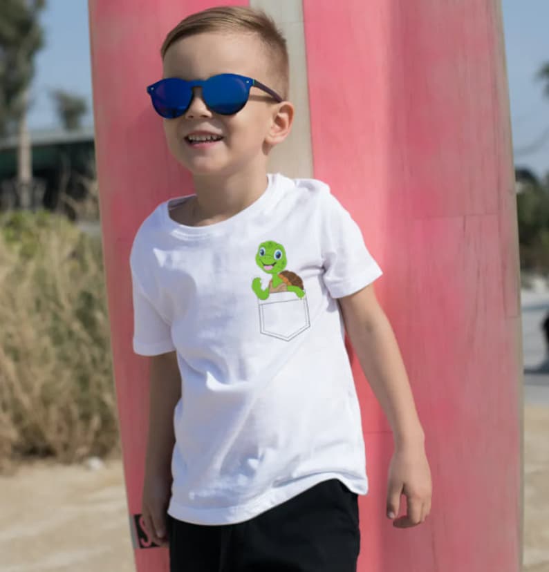 May include: A white t-shirt with a green turtle in the pocket. The turtle is smiling and has its arms raised. The shirt is being worn by a young boy wearing blue sunglasses.