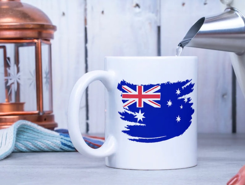 May include: White ceramic mug with a blue, red, and white Australian flag design. The flag is painted in a brushstroke style.
