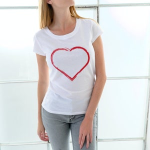 May include: A white t-shirt with a red heart design on the front. The heart is outlined in red and is a simple, hand-drawn design.