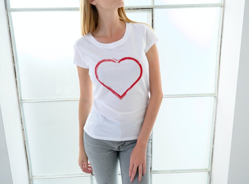 May include: A white t-shirt with a red heart design on the front. The heart is outlined in red and is a simple, hand-drawn design.