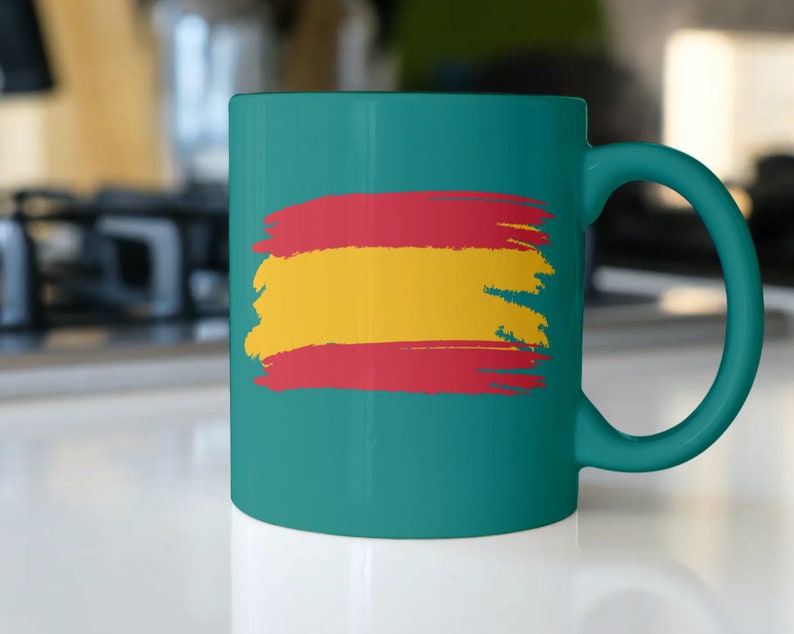 May include: A teal ceramic mug with a painted Spanish flag design. The flag is red, yellow, and red with a brushstroke effect.
