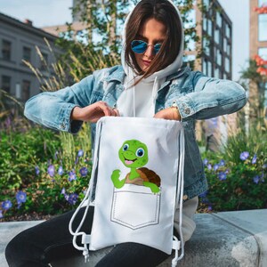 May include: White drawstring bag with a cartoon turtle peeking out of a pocket. The turtle is green with a brown shell and has a big smile.