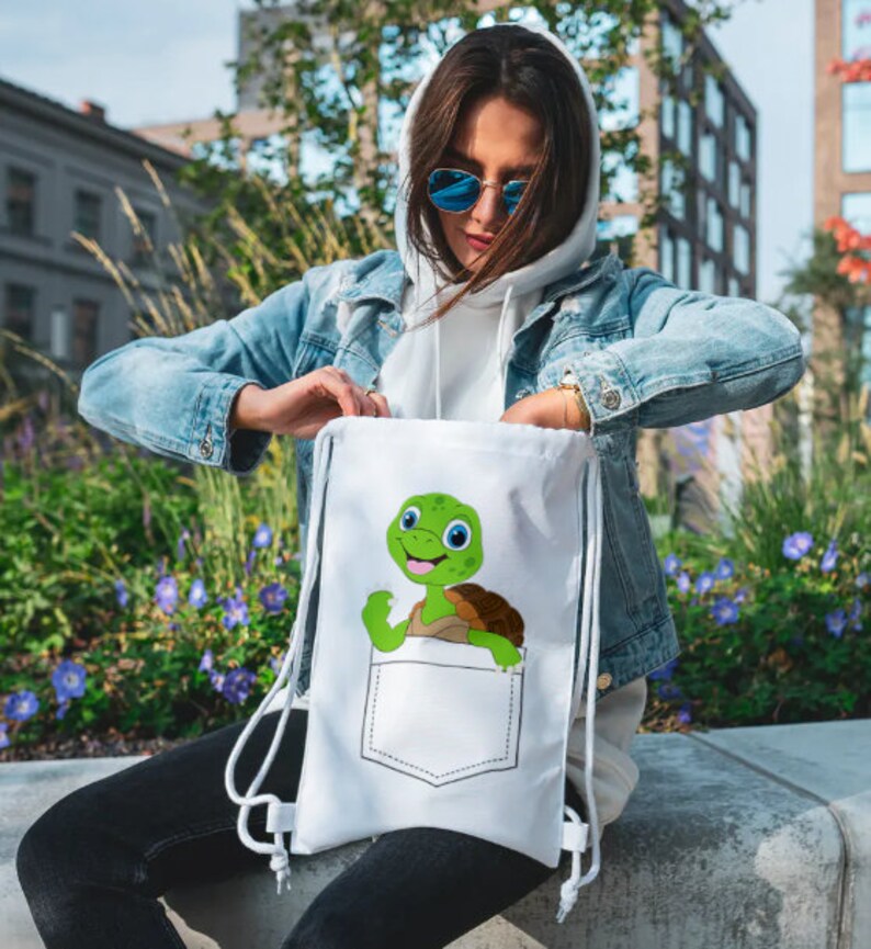 May include: White drawstring bag with a cartoon turtle peeking out of a pocket. The turtle is green with a brown shell and has a big smile.