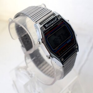 K&ouml;nnte beinhalten: Eine silberfarbene Montana Digitaluhr mit schwarzem Zifferblatt, das die Uhrzeit anzeigt. Die Uhr hat ein rechteckiges Geh&auml;use mit blauen und roten Akzenten. Das Armband besteht aus silberfarbenen Metallgliedern.