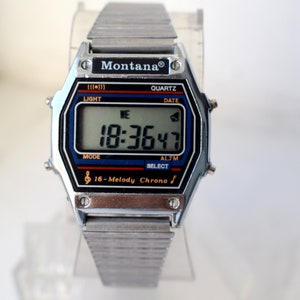 K&ouml;nnte beinhalten: Silberfarbene Montana Quartz Digitaluhr mit rechteckigem Zifferblatt. Die Uhr zeigt Uhrzeit, Datum und andere Funktionen auf einem digitalen Bildschirm an. Das Armband besteht aus silberfarbenen Metallgliedern. Auf dem Zifferblatt steht "Montana", "Quartz" und "16-Melody Chrono".