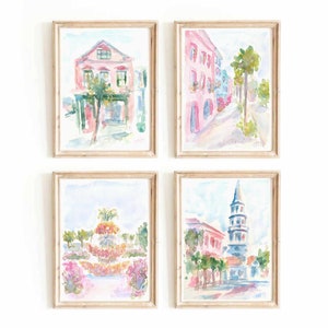 May include: Set of four watercolor paintings depicting scenes from Charleston, South Carolina. The paintings feature pastel pink and blue hues and depict a pink building with a palm tree, a street lined with pastel pink buildings, a park with a fountain, and a church steeple.