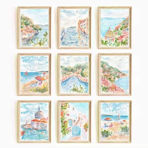 May include: Nine watercolor paintings of a coastal town with buildings, boats, and the ocean. The paintings are framed in light wood and arranged in a grid pattern on a white wall.