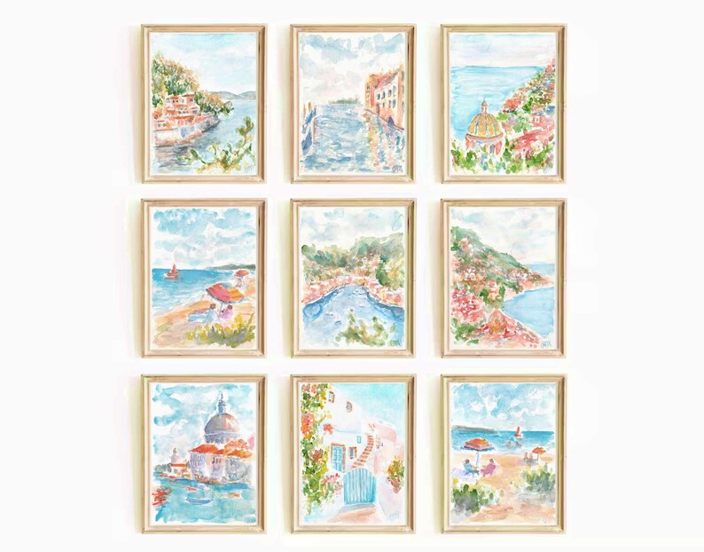 May include: Nine watercolor paintings of a coastal town with buildings, boats, and the ocean. The paintings are framed in light wood and arranged in a grid pattern on a white wall.