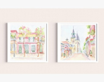 May include: Two watercolor paintings of New Orleans street scenes. The first painting shows a pink building with a balcony and green trees. The second painting shows a street with a church in the background.