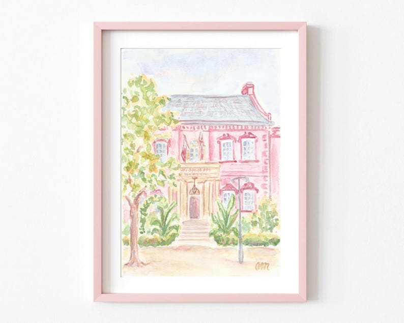 May include: Watercolor painting of a pink house with a white door and windows. The house is surrounded by green trees and bushes. The painting is framed in a light pink frame.