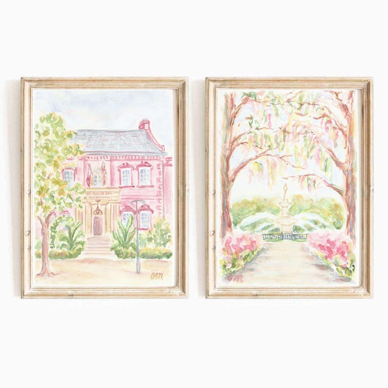 May include: Two watercolor paintings in light wood frames. The left painting shows a pink house with white trim and green trees. The right painting shows a path leading to a fountain in a park with pink flowers and trees.