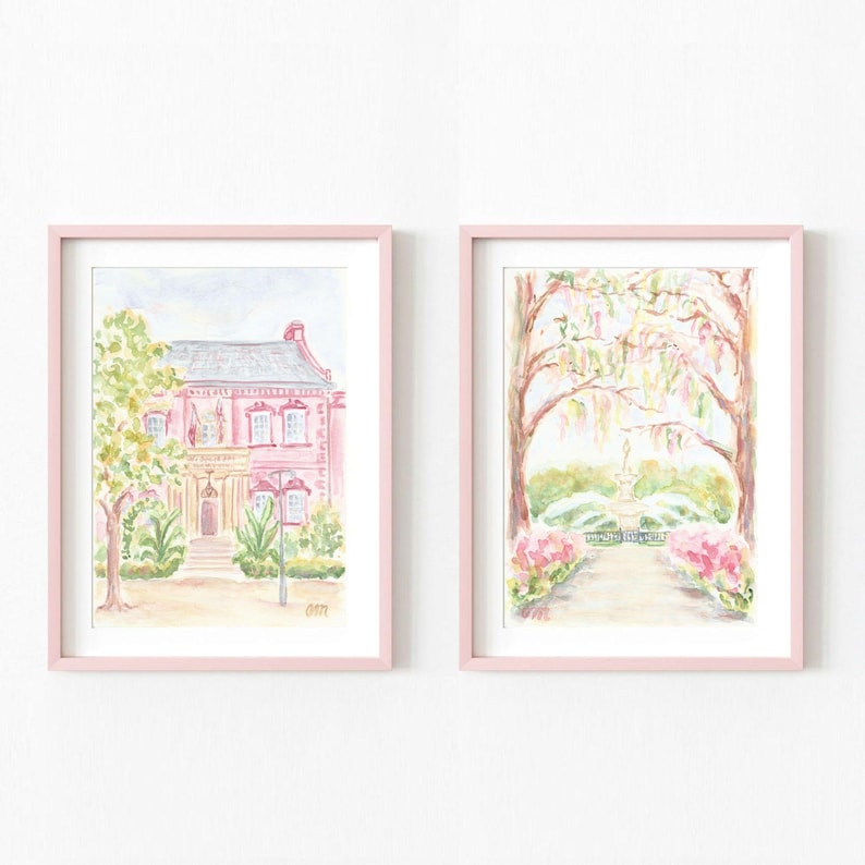 May include: Two watercolor paintings in pink frames. The first painting shows a pink house with a yellow door and green trees. The second painting shows a path leading to a fountain with trees and flowers.