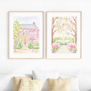 May include: Two watercolor paintings in wooden frames. The first painting shows a pink house with a green tree in front. The second painting shows a path leading to a fountain with trees and flowers on either side.
