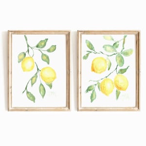 Peut inclure: Deux peintures à l'aquarelle encadrées représentant des branches de citron avec des feuilles vertes et des citrons jaunes. Les peintures sont dans des cadres simples en bois clair.