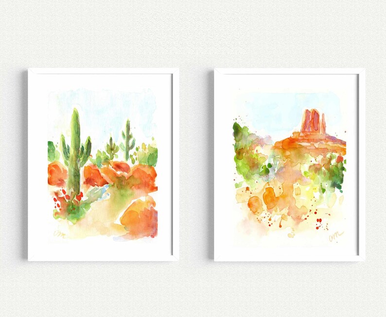 May include: Two watercolor paintings of desert landscapes. The first painting shows a tall cactus with smaller cacti and red rocks. The second painting shows a red rock formation with green bushes and a blue sky.
