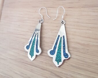 May include: A pair of silver dangle earrings with a geometric design. The earrings are decorated with blue and green stones.