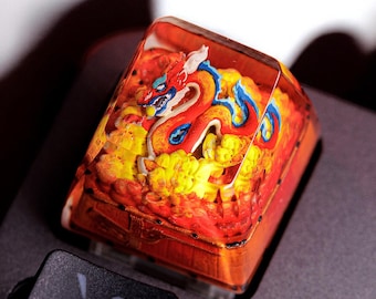 May include: A custom keyboard keycap featuring a detailed dragon design. The keycap is primarily orange with a vibrant dragon in red, blue, and yellow. The keycap is installed on a black keyboard, with other keys visible in the foreground.