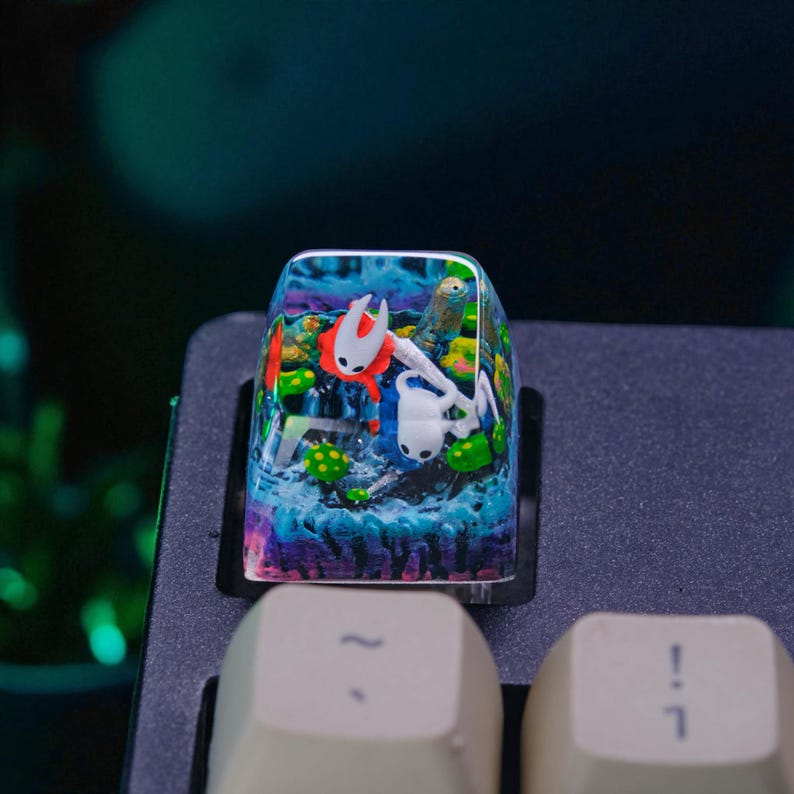 May include: A custom keyboard keycap featuring a colorful, detailed resin design. The keycap showcases a fantasy scene with characters in a vibrant underwater setting, with shades of blue, green, and red. The keycap is mounted on a black keyboard.