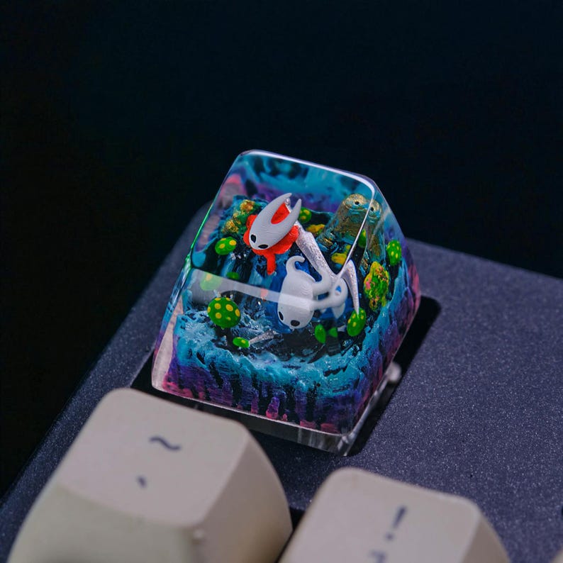May include: A custom artisan keycap featuring a vibrant underwater scene with two white and red characters. The keycap is clear with a colorful, layered design, including blue, green, and purple hues, and is mounted on a keyboard.