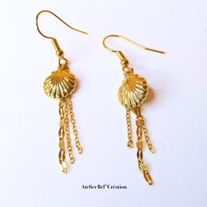Peut inclure: Boucles d'oreilles dorées avec un motif de coquillage et des chaînes pendantes.