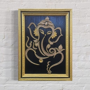 Puede incluir: Una obra de arte enmarcada que representa la deidad hindú Ganesha, con intrincados detalles dorados sobre un fondo negro.