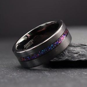 Könnte beinhalten: Ein schwarzer Wolframkarbidring mit einem farbenfrohen Inlay aus lila, blauem und rotem glitzerndem Material. Der Ring hat eine gebürstete Metalloberfläche und die Worte "Tungsten Carbide" sind seitlich eingraviert.