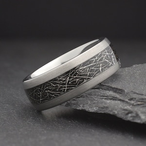 May include: A silver and black tungsten carbide ring with a textured black band. The ring has a brushed silver finish.