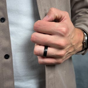 Hand wearing a black titanium ring with a blurred background
