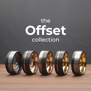May include: Five different men's wedding bands with a black and gold offset design. The bands are arranged in a row from left to right. The band on the left has a blue stripe. The text "the Offset collection" is displayed above the bands.