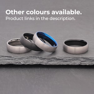 May include: Three different colored rings on a dark gray surface. The rings are all the same width and have a brushed finish. The rings are silver, black, and blue.