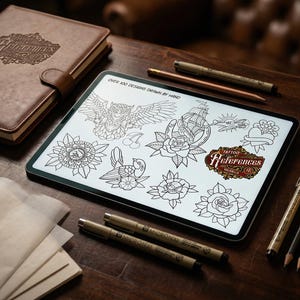 May include: A digital tablet displays tattoo design references, including an owl, ship, and roses. A leather-bound notebook, pens, and pencils are arranged on a wooden surface. The tablet features the text "Over 100 Designs Drawn By Hand" and "Tattoo References Valhalla".